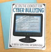Poster warning about cyber bullying with a computer monitor graphic on a wooden surface.