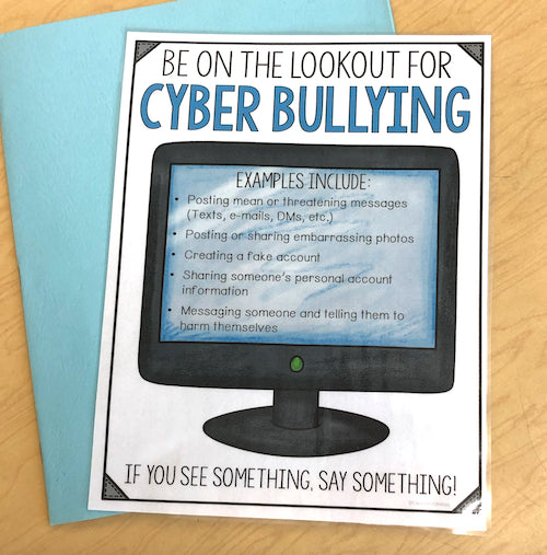 Poster warning about cyber bullying with a computer monitor graphic on a wooden surface.
