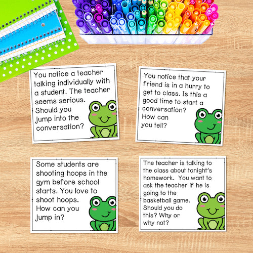 Educational cards with frog illustrations and scenarios on a wooden surface with markers in the background.