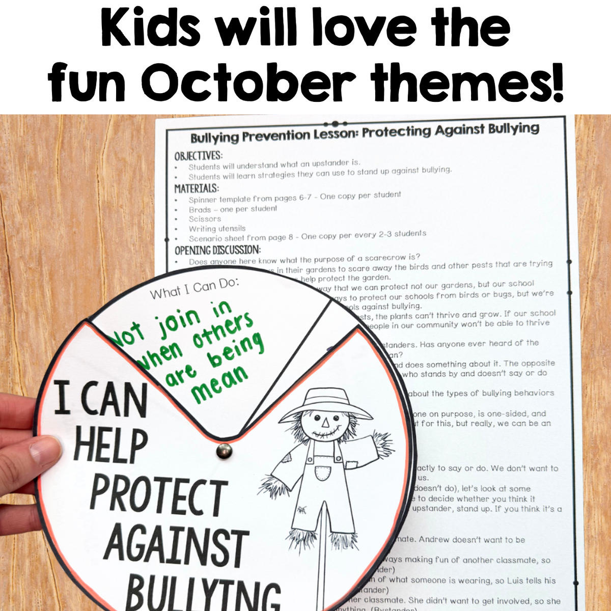 A hand holds a green and white spinner card over a printed bullying prevention lesson sheet on a wooden desk. Large headline text at the top reads, 'Kids will love the fun October themes!'.