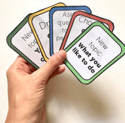Hand holding educational flashcards with various prompts on a plain background