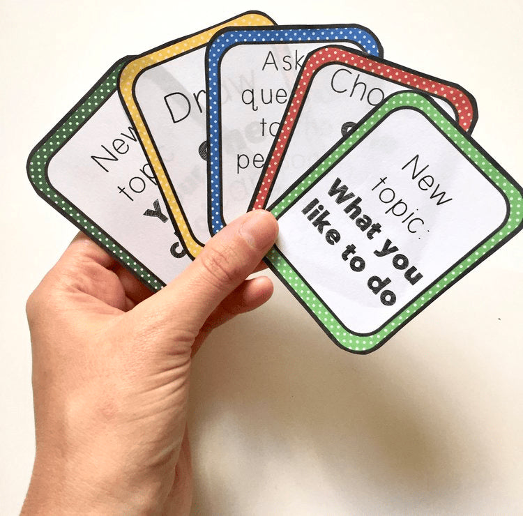 Hand holding educational flashcards with various prompts on a plain background