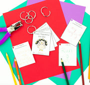 Colorful paper with keychains, a hole punch, and writing materials on a multicolored background